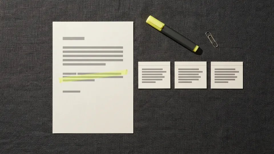A printed web page with one sentence highlighted beside three small citation cards and a highlighter pen on a charcoal desk