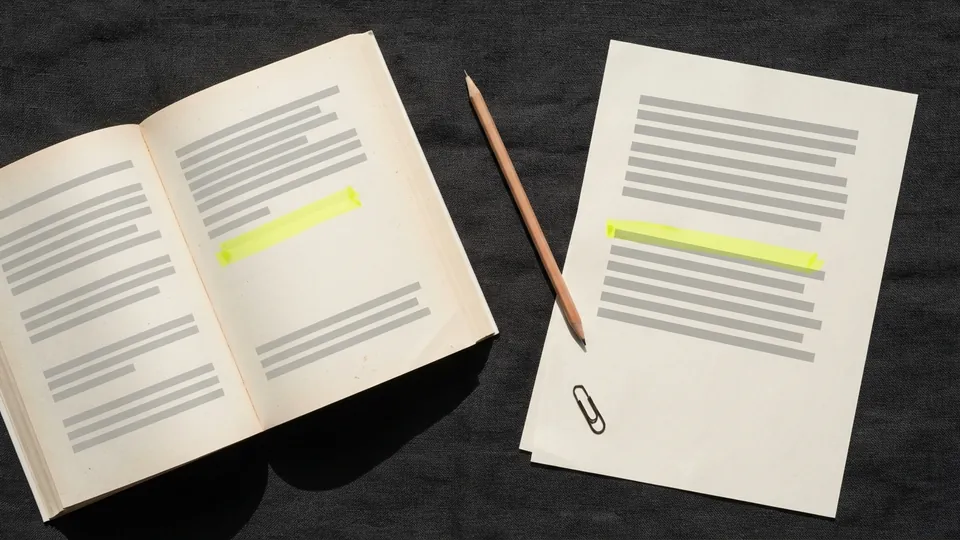 An open book and an essay sheet on a charcoal desk, the same short passage highlighted in yellow on both, a pencil between them