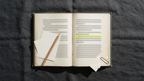 An old clothbound book open on a desk with one line highlighted in yellow and a blank index card and pencil resting on the page