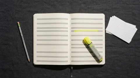 A ruled reading log notebook open on a charcoal desk, one row highlighted in yellow, a highlighter pen resting on the page and index cards beside it