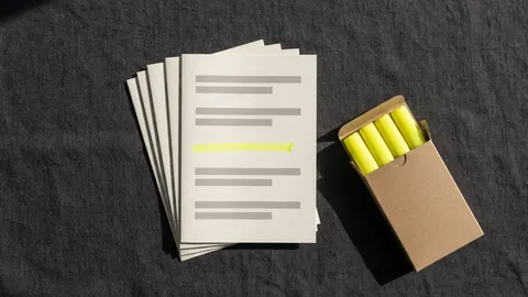 A fanned stack of printed handouts with one line marked on the top copy, beside a box of yellow highlighters