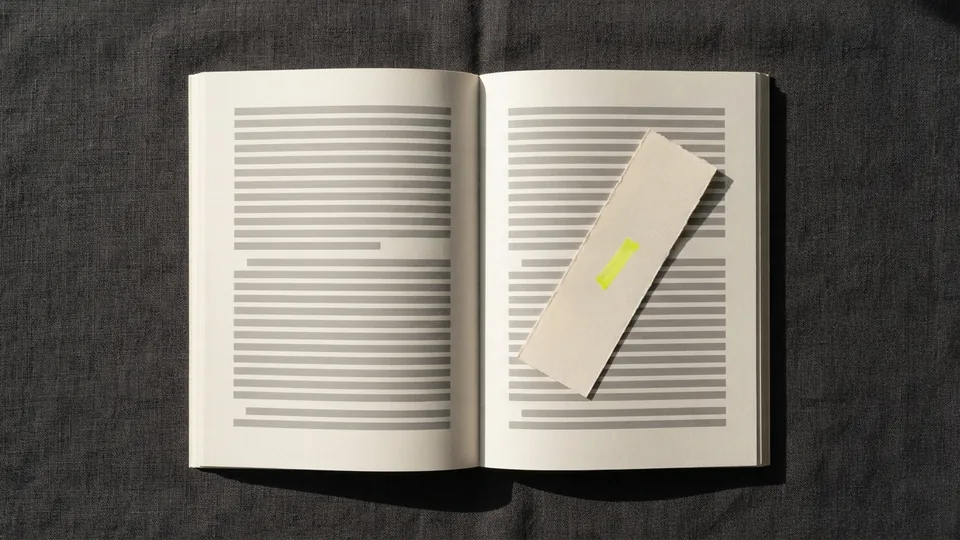 A paper bookmark with a small yellow mark lying across an open book