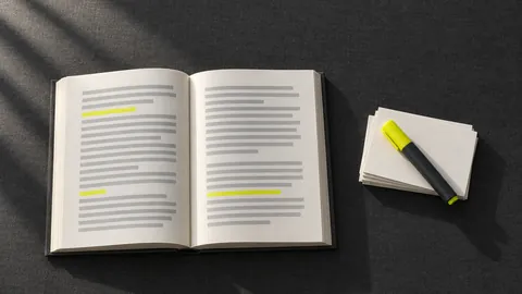 An open book with a few short lines marked in yellow, next to a stack of blank index cards and a highlighter
